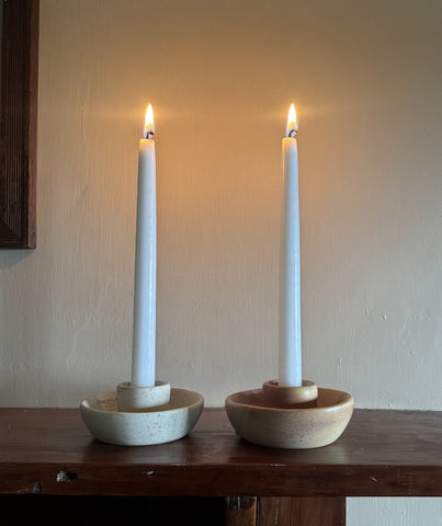 Pink Kenyan soapstone taper candle holder with a lit candle against green botanical wallpaper