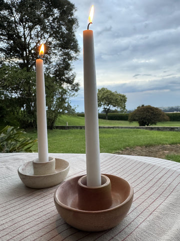 Pink Kenyan soapstone taper candle holder with a lit candle against green botanical wallpaper