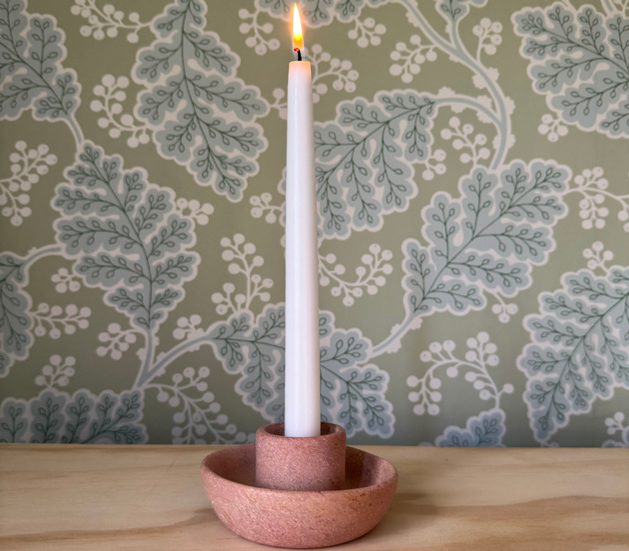 Pink Kenyan soapstone taper candle holder with a lit candle against green botanical wallpaper
