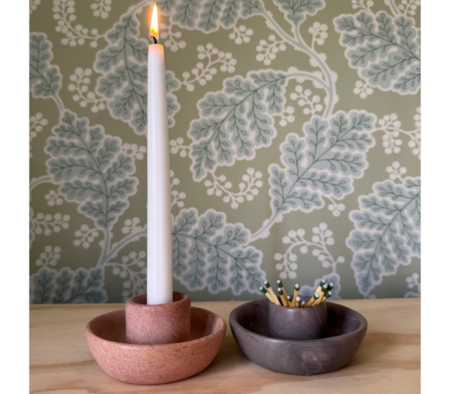 Pink soapstone candle holder with lit taper beside a gray holder used for matches
