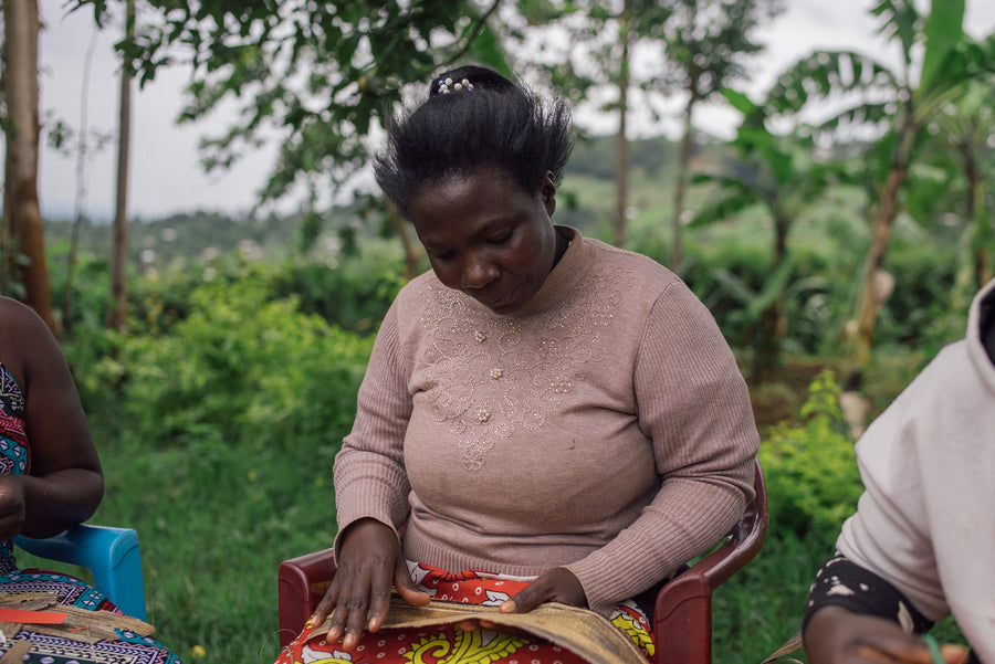 An Ajiri artisan smoothing sheets of dried banana bark on her lap