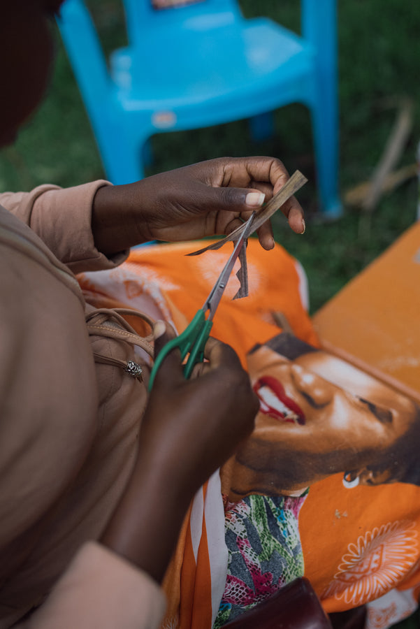 An Ajiri artisan cutting a shape from dried banana bark with scissors