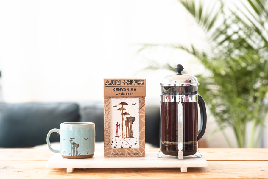Box of Ajiri Kenyan AA whole bean coffee between a blue elephant mug and a French press of coffee